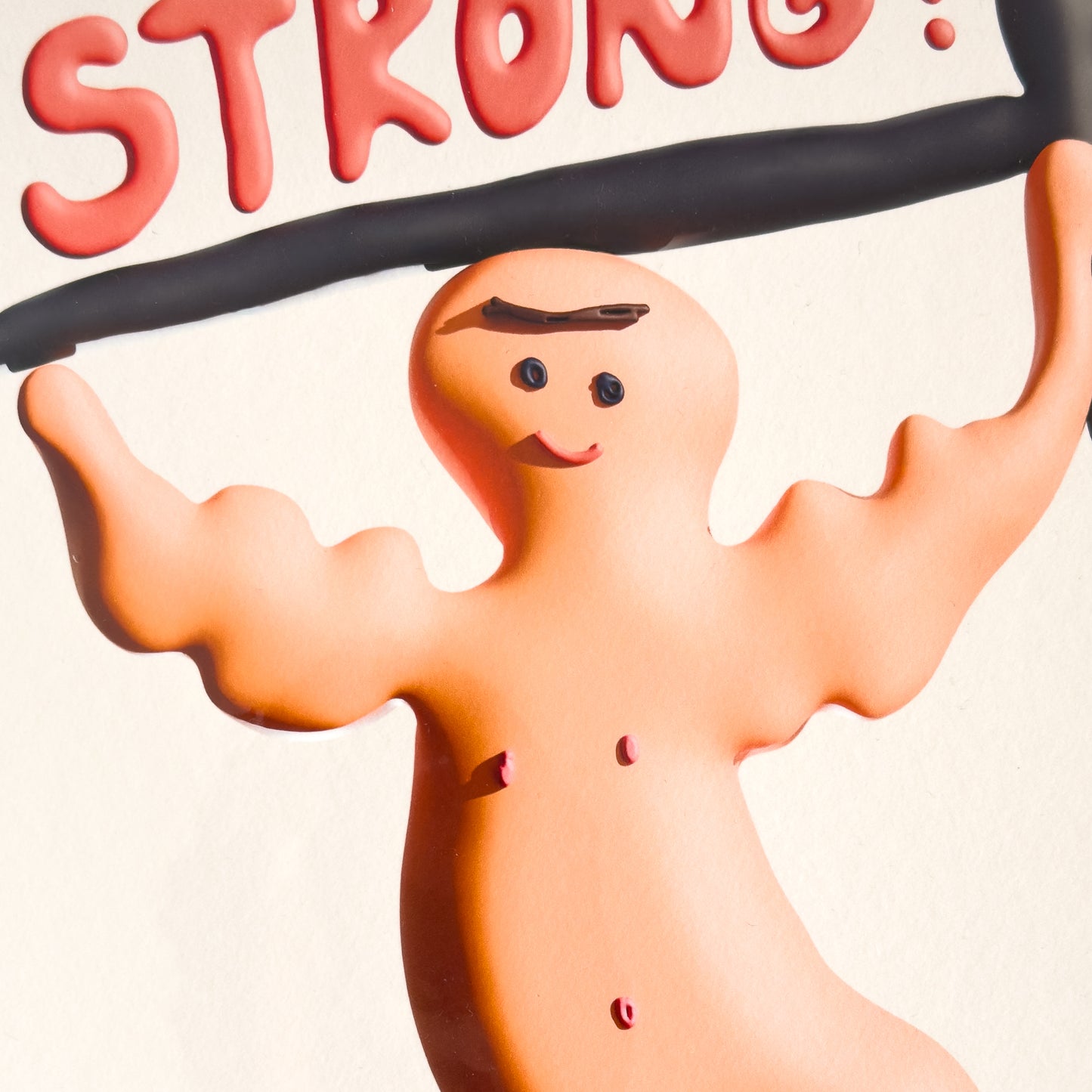 A close up of an art print with a cartoon character lifting weights and the word 'STRONG!' on a plain background.