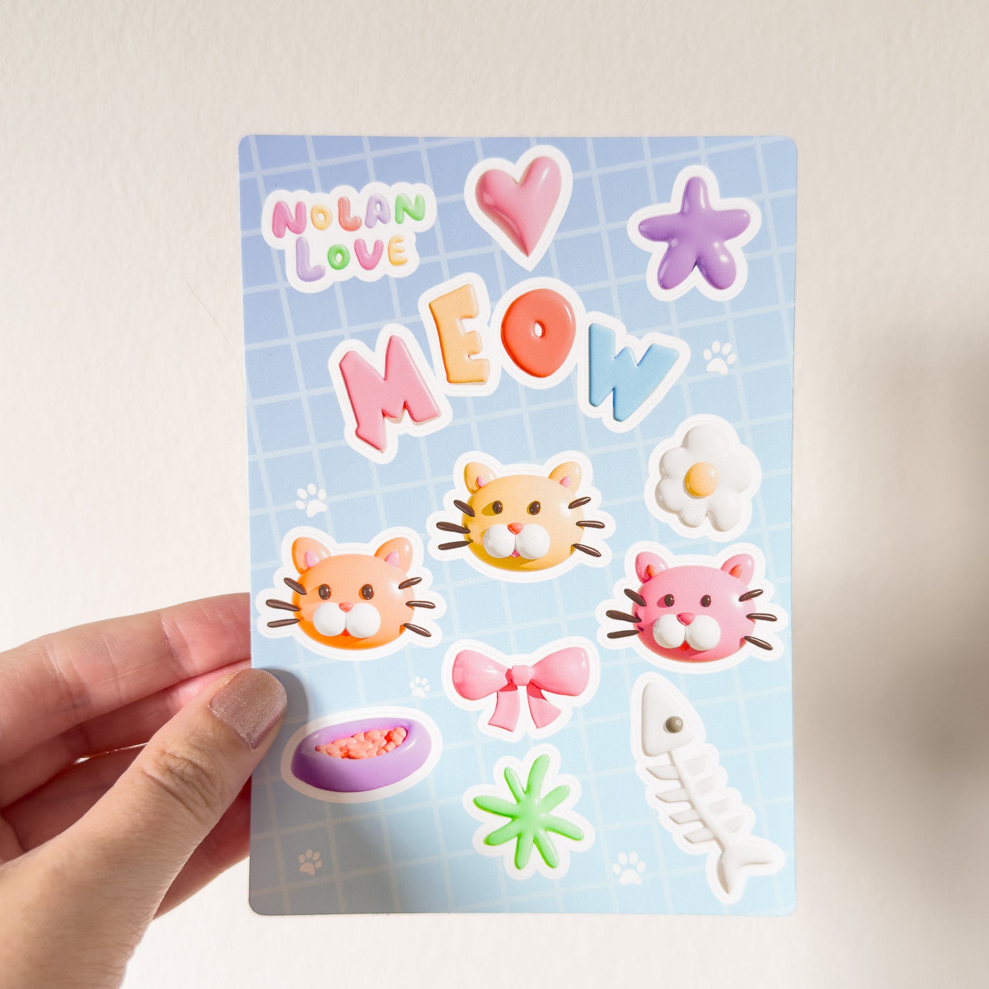 Sheet of colorful stickers with cat-themed designs held by a hand against a light background