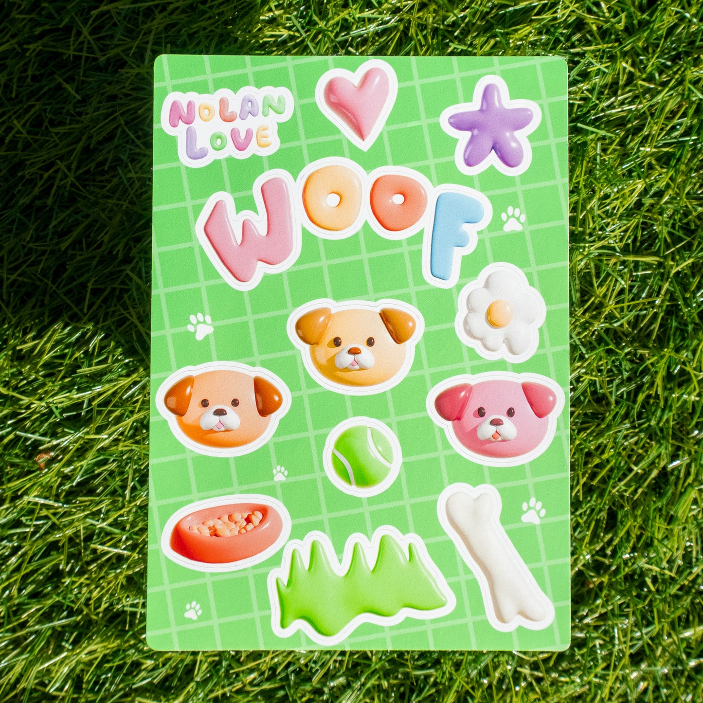 Sheet of colorful stickers with dog-themed designs on a green grid background, placed on grass.