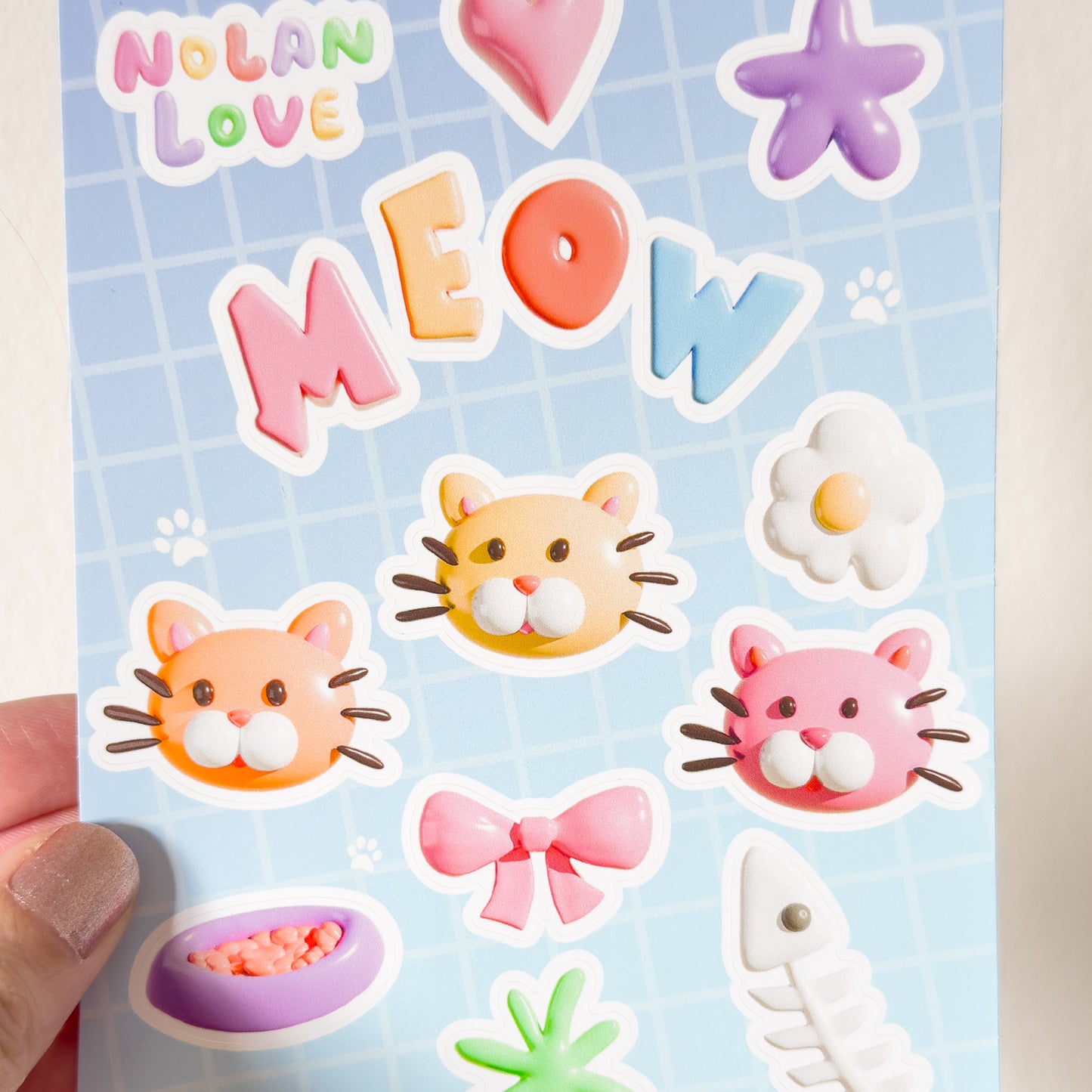 A close up of a hand holding a sheet of colorful stickers with cat-themed designs held by a hand against a light background.