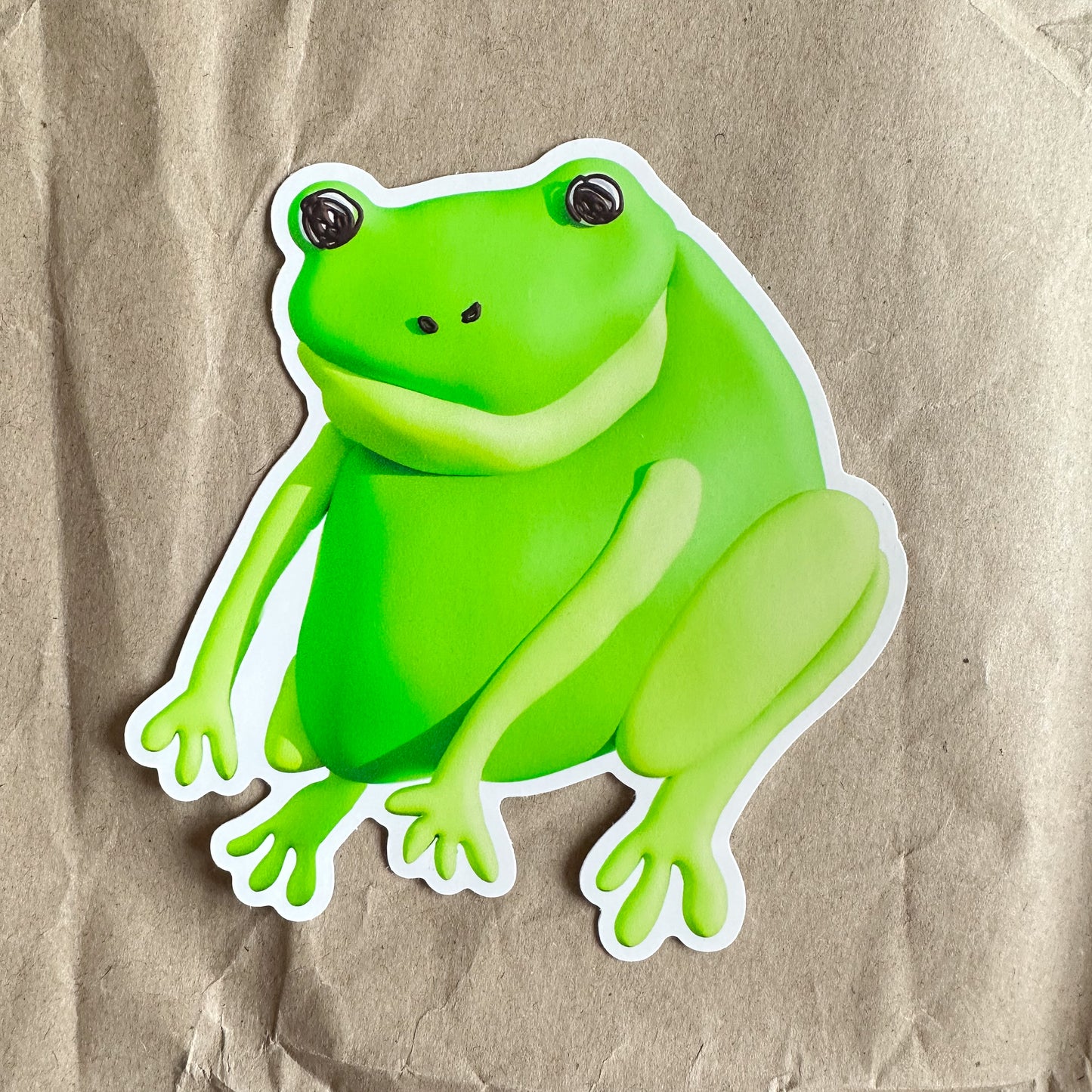 A large green frog sticker sits on a brown paper background.